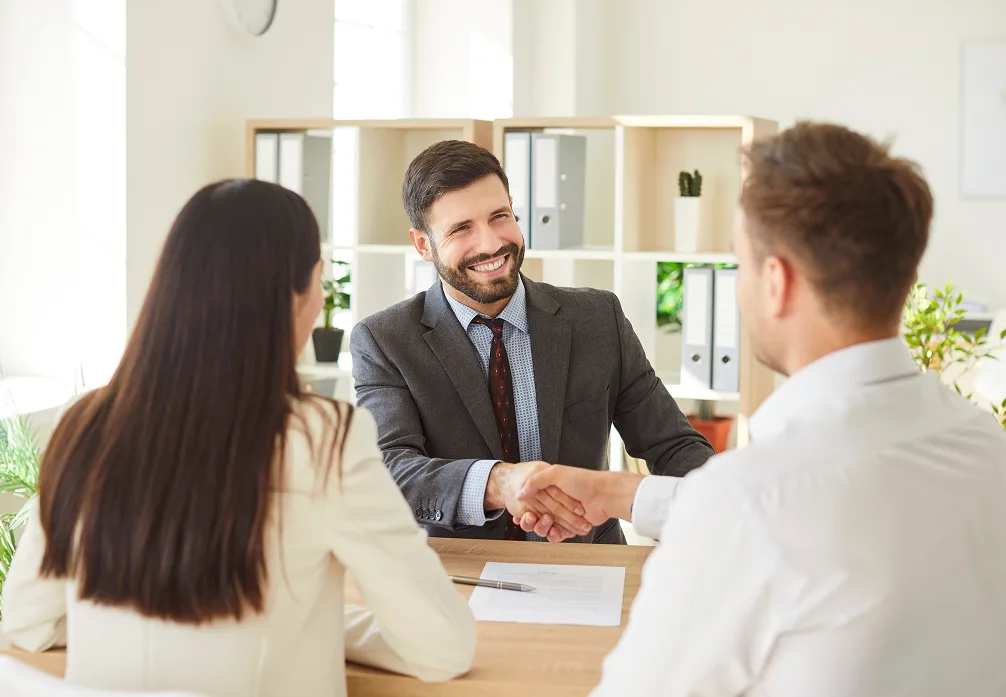 Two people shaking hands across a desk in an office