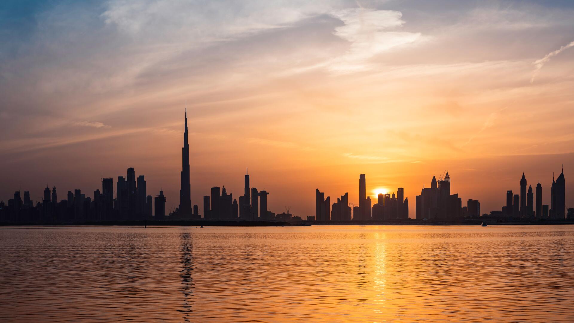 Dubai skyline at sunset seen across the water, with the Burj Khalifa